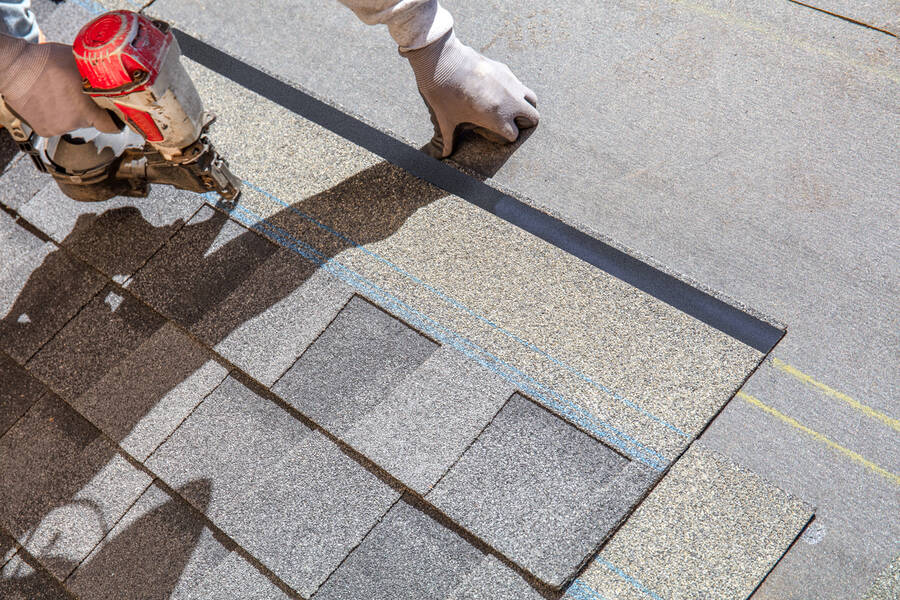 Roofing contractor installing asphalt shingles with a nail gun on a residential roof